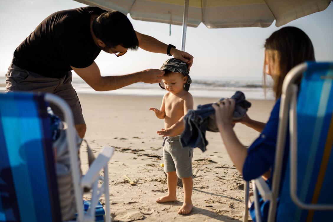 Besser geschützt sind Kinder am Strand durch bedeckende UV-Kleidung, Sonnenbrille und einen breitkrempigen Hut.  / Foto: Getty Images/Capuski