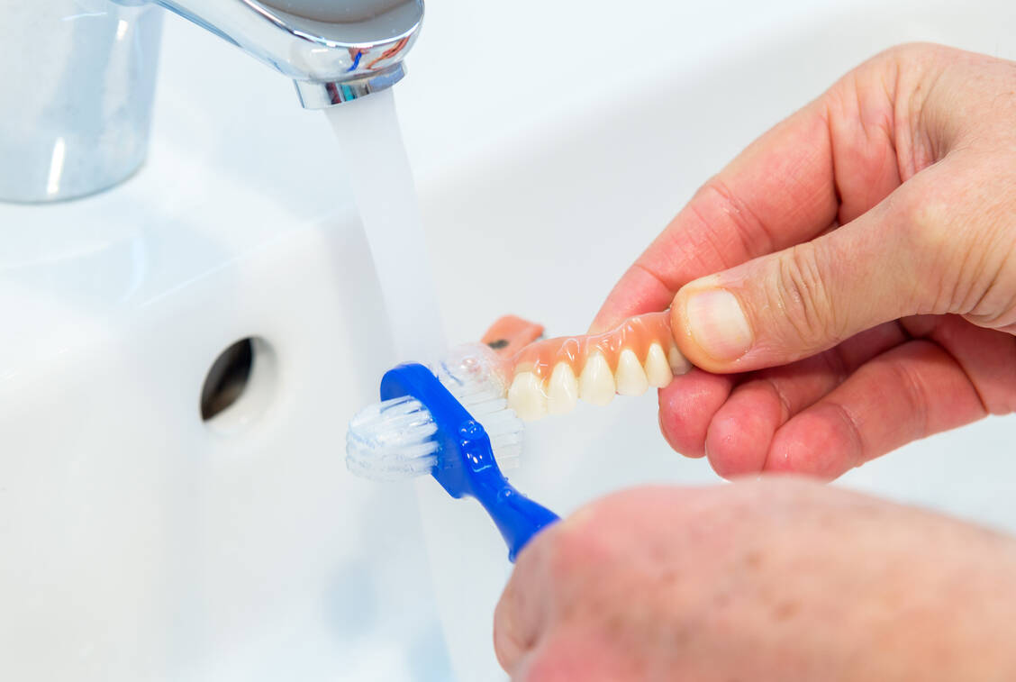 Ein Handtuch ins Waschbecken legen beim Putzen vermindert die Bruchgefahr, wenn einem die nasse Prothese aus der Hand fällt. / Foto: Adobe Stock/nemo1963
