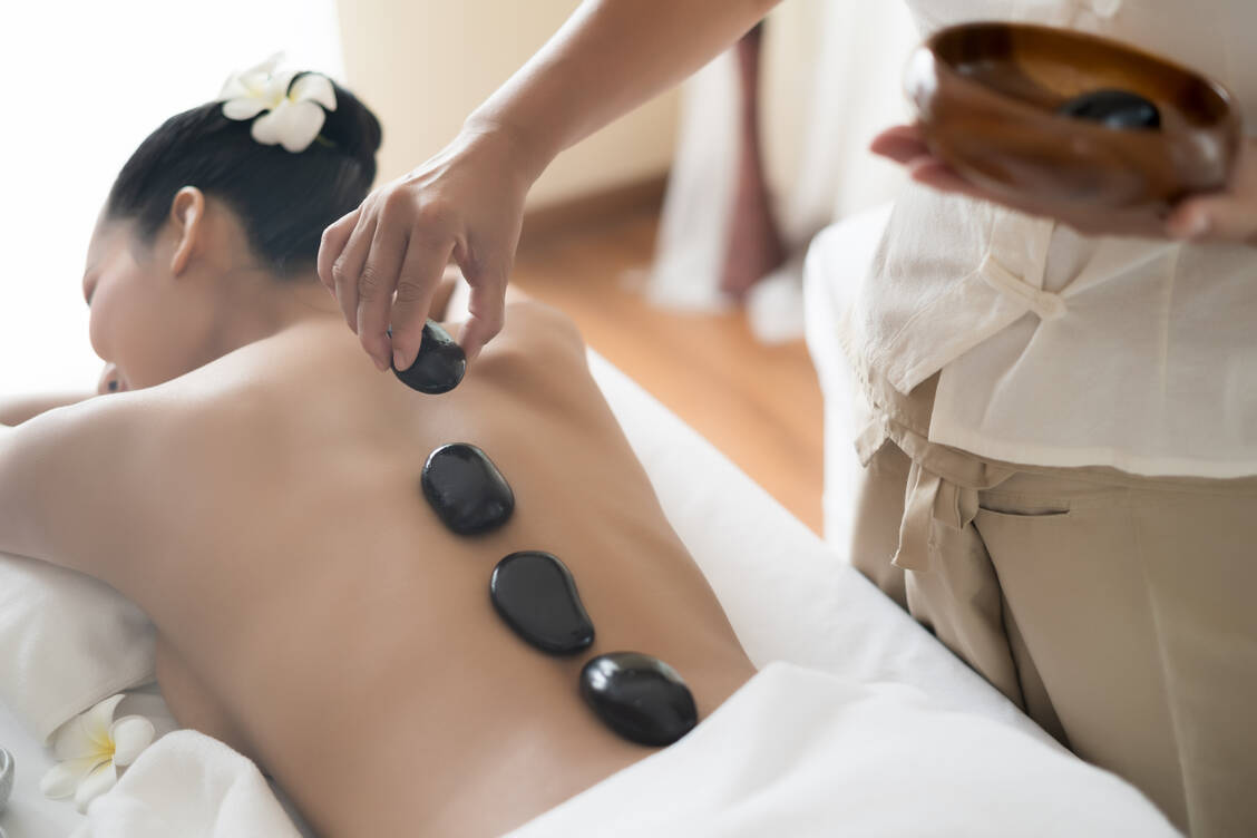 Bei einer Hot-Stone-Massage platziert der Therapeut warmen, unterschiedlich geformte Steine auf dem Rücken. / Foto: Getty Imgages/
Thianchai Sitthikongsak