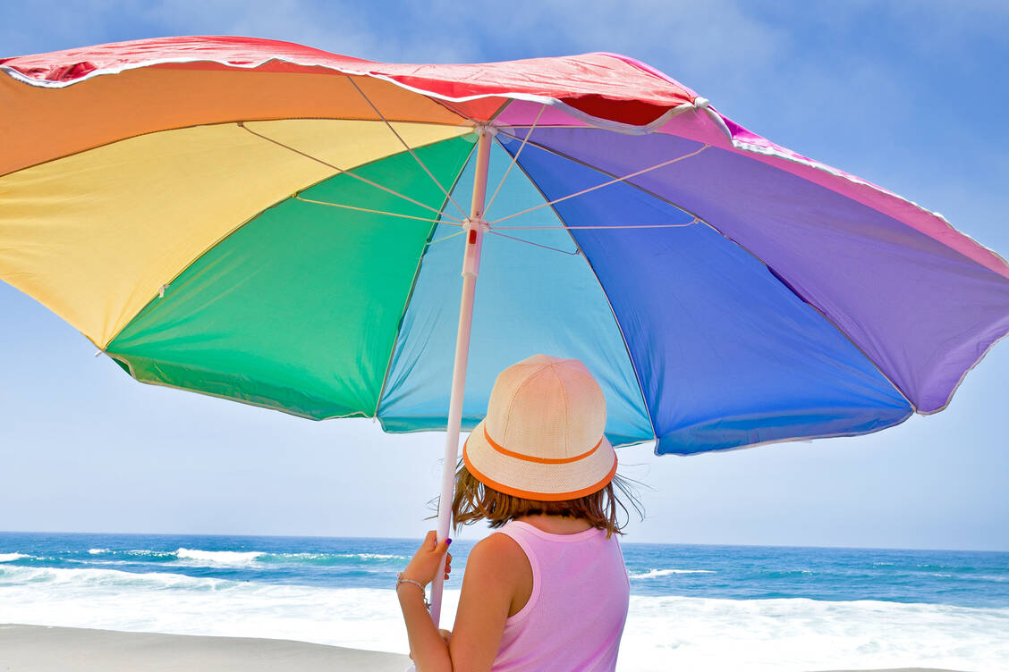 Gut behütet an den Strand: Dafür sorgen ein Sonnenschirm, eine Kopfbedeckung und ausreichend Sonnencreme.  / Foto: Getty Images/Geri Lavrov