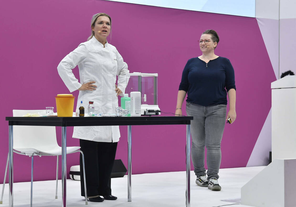 Dr. Sandra Barisch als zweifelnde PTA und Dr. Julia Potschadel als »freundliches und mahnendes Gewissen« im Hintergrund beim Live-Cooking auf der Expopharm 2022 / Foto: Avoxa/Expopharm