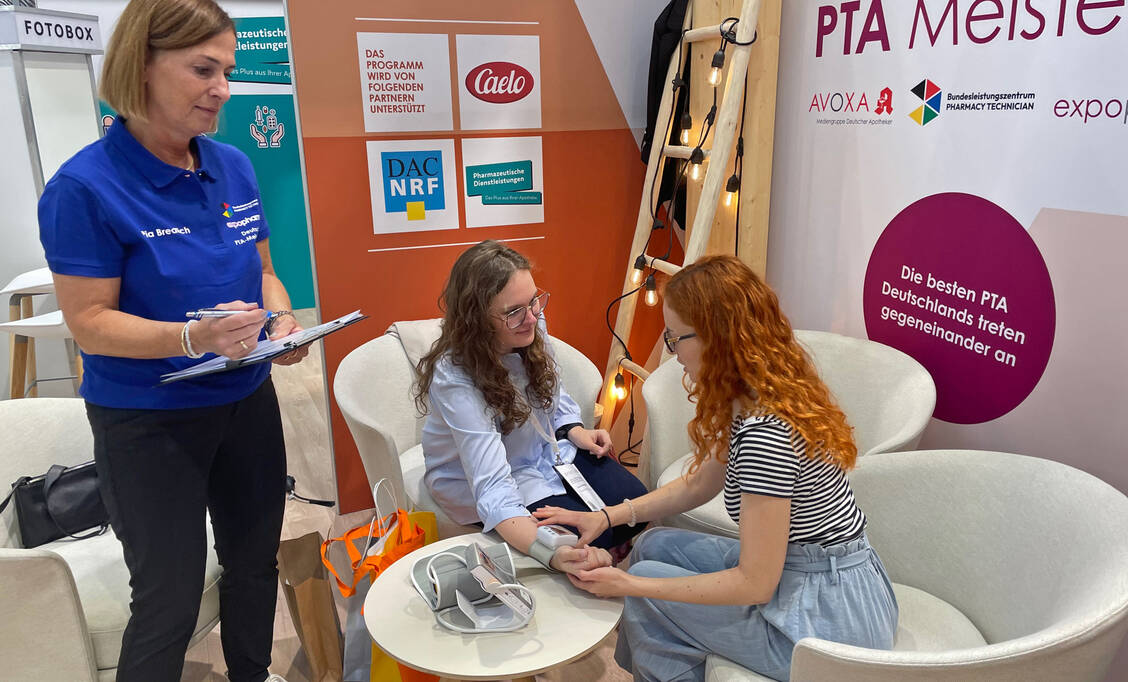 Üben für das Finale: Die PTA und Meisterschafts-Finalistinnen Laura Baitinger und Regina Babel zeigen, wie der Blutdruck fachlich korrekt gemessen wird.  / © PZ/Verena Schmidt