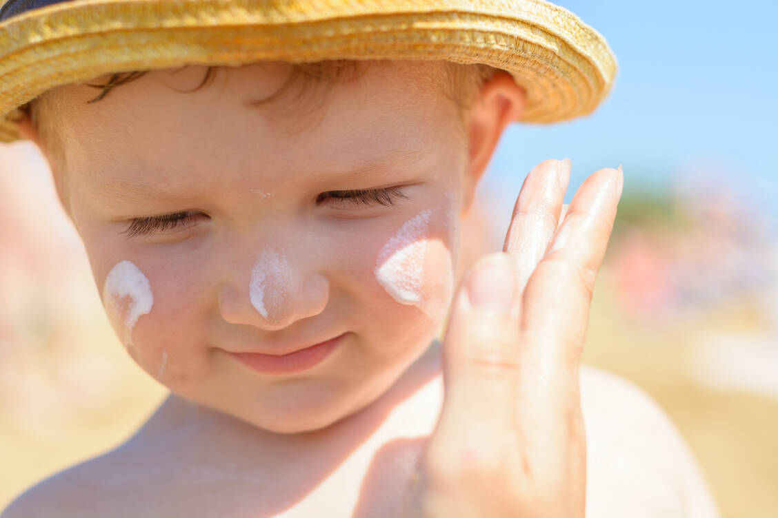 Auch wenn Kinder sich oft mit Händen und Füßen gegen das Eincremen wehren – es muss sein, damit die Haut nicht irreversibel Schaden nimmt. / © Adobe Stock/Alexander Penyushkin